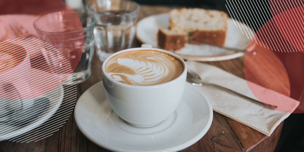 Xícara de café sobre mesa de madeira ao lado de um pedaço de bolo servido em prato branco